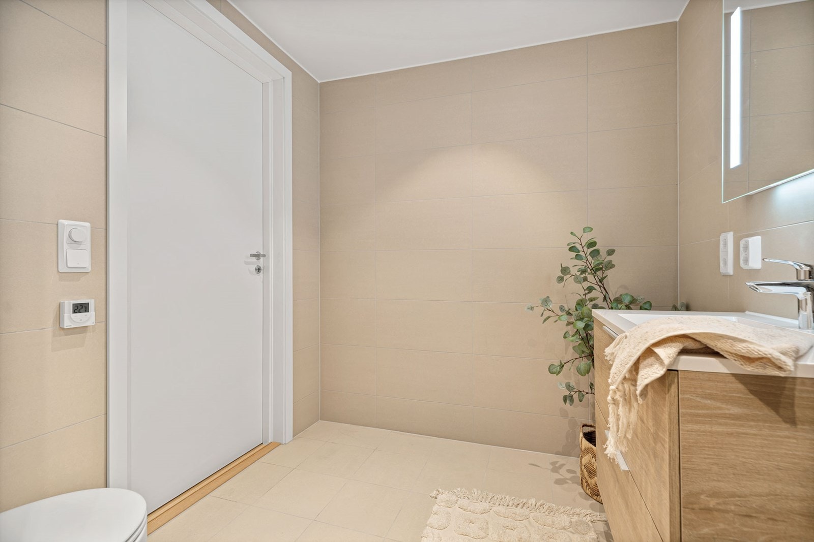 Badet er romslig og er innredet med veggmontert toalett, stor dusjsone, heldekkende servant i fin baderomsinnredning og opplegg til vaskemaskin Galleribilde