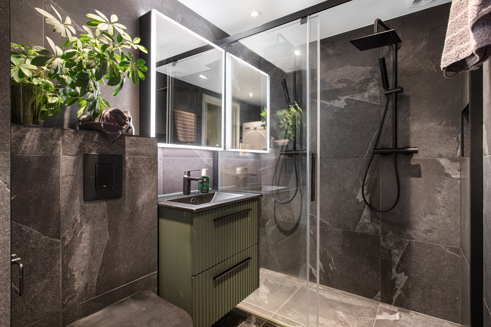 Delikat, flislagt bad med mørke overflater, regnfallsdusj og speilskap med belysning. Galleribilde