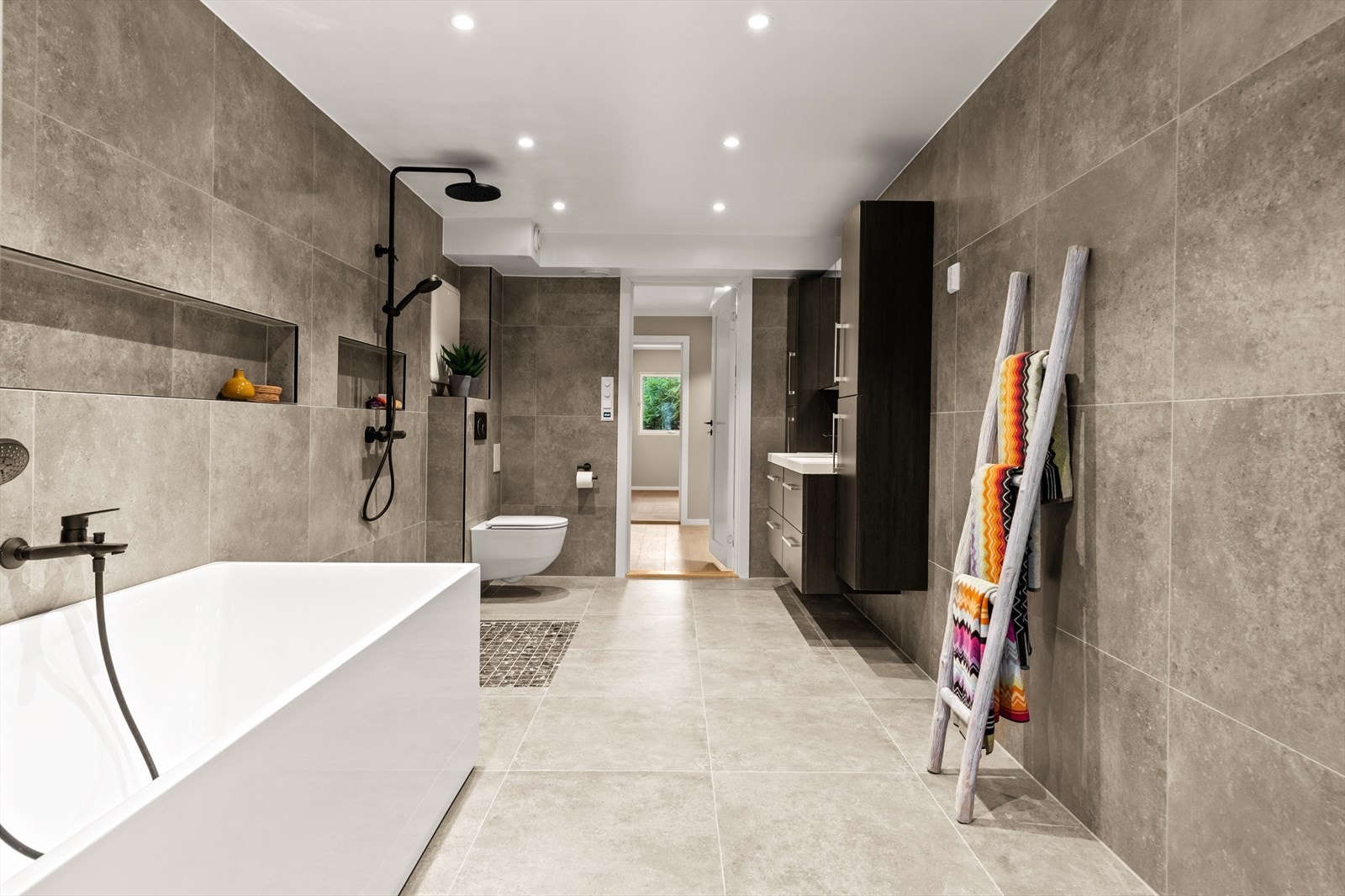 Baderomsinnredning bestående med slette, mørke fronter og overhengende skap med speil, 2 nedfelte servanter og 2 høyskap, veggmontert toalett og badekar. Opplegg og plass til vaskemaskin. Mekanisk avtrekk. Galleribilde