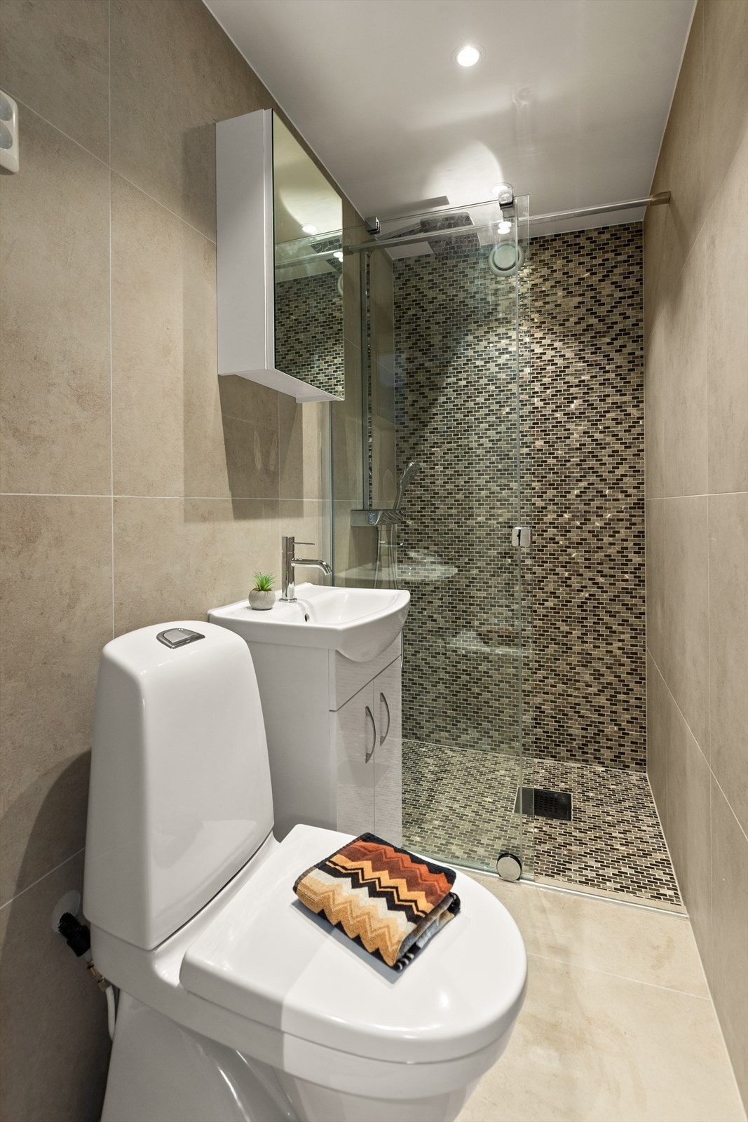 Flott bad tilliggende entréen med flislagte overflater på gulv og vegger med elektriske varmekabler i gulv.
Baderomsinnredning bestående av nedfelt servant, toalett og dusjvegger/hjørne. Mekanisk avtrekk. Galleribilde