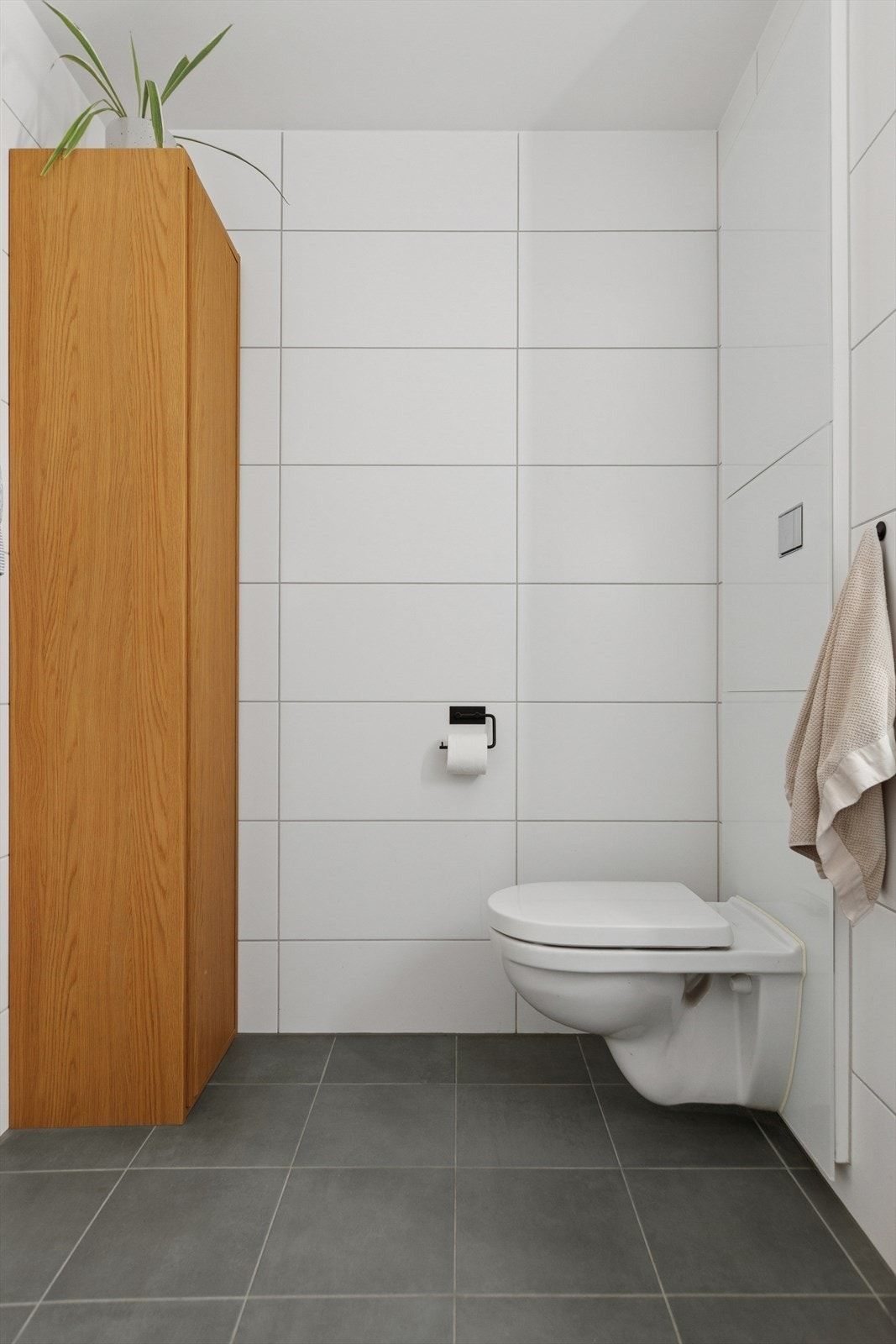 Badet er innredet med vegghengt toalett, servant, opplegg for vaskemaskin og åpen dusjsone med dusjgarnityr på vegg. Galleribilde