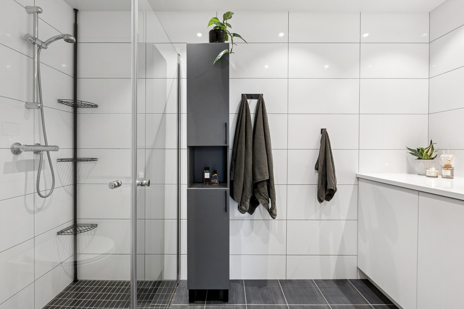 Innredningen består av gulvmontert servantskap med heldekkende servant, speil med stikkontakter, dusjhjørne med innfellbare glassdører og vegghengt toalett med innebygd sisterne. Galleribilde