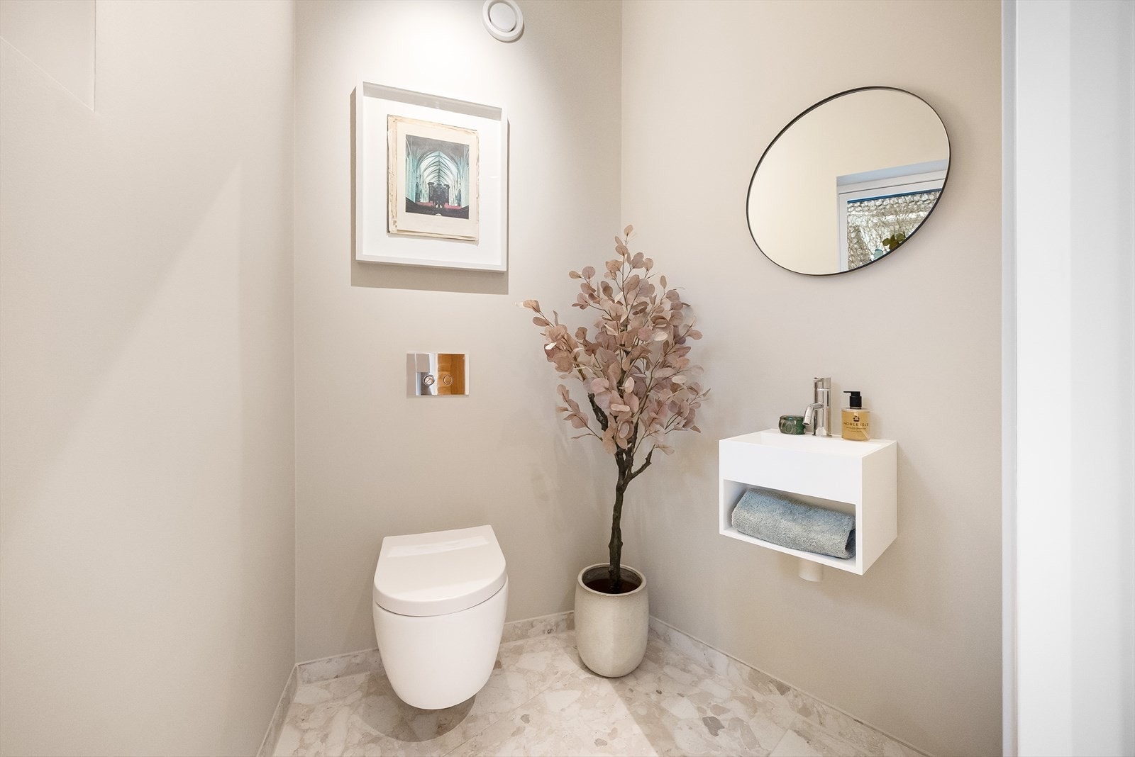 Flislagt gulv med varme, veggfestet toalett og servant med speil på vegg Galleribilde