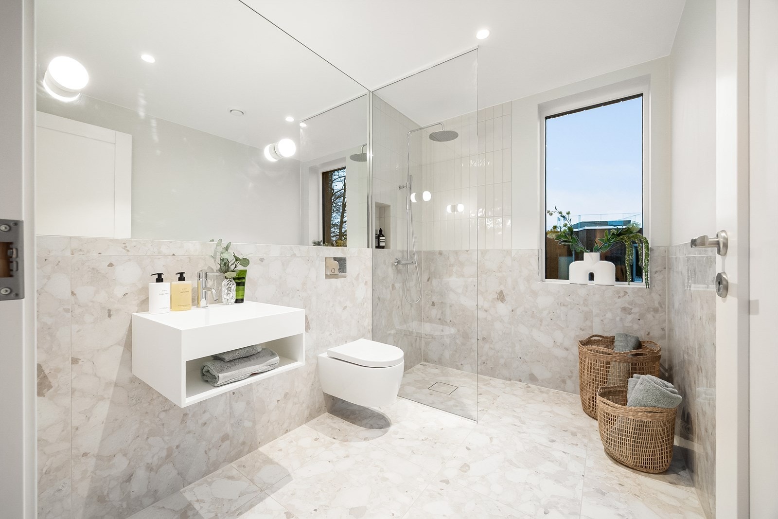 Familiebad med flislagte overflater, varme i gulvet, dusjsone med glassvegg og stort veggspeil Galleribilde