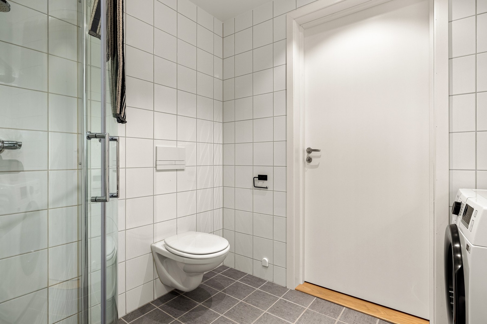 Badet er innredet med vegghengt toalett, servant med innredning, dusj m/glassvegger og opplegg for vaskemaskin. Galleribilde