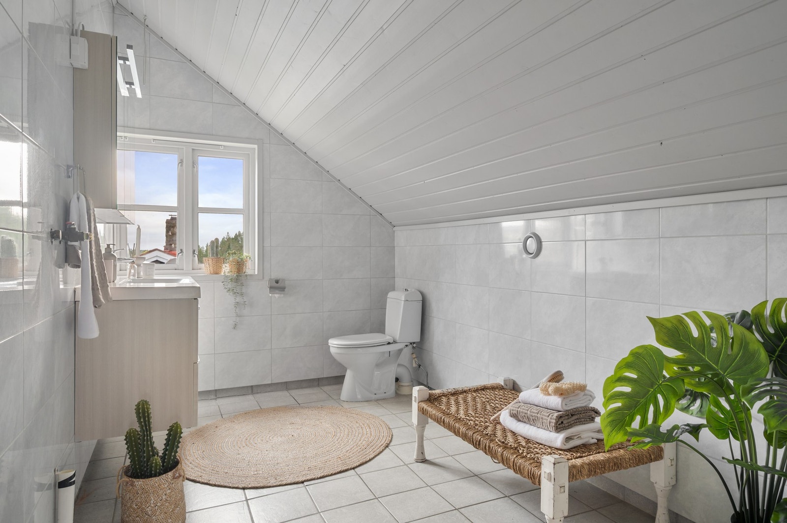 Flislagt bad med opplegg til vaskemaskin, gulvmontert toalett og servant i skap. Galleribilde