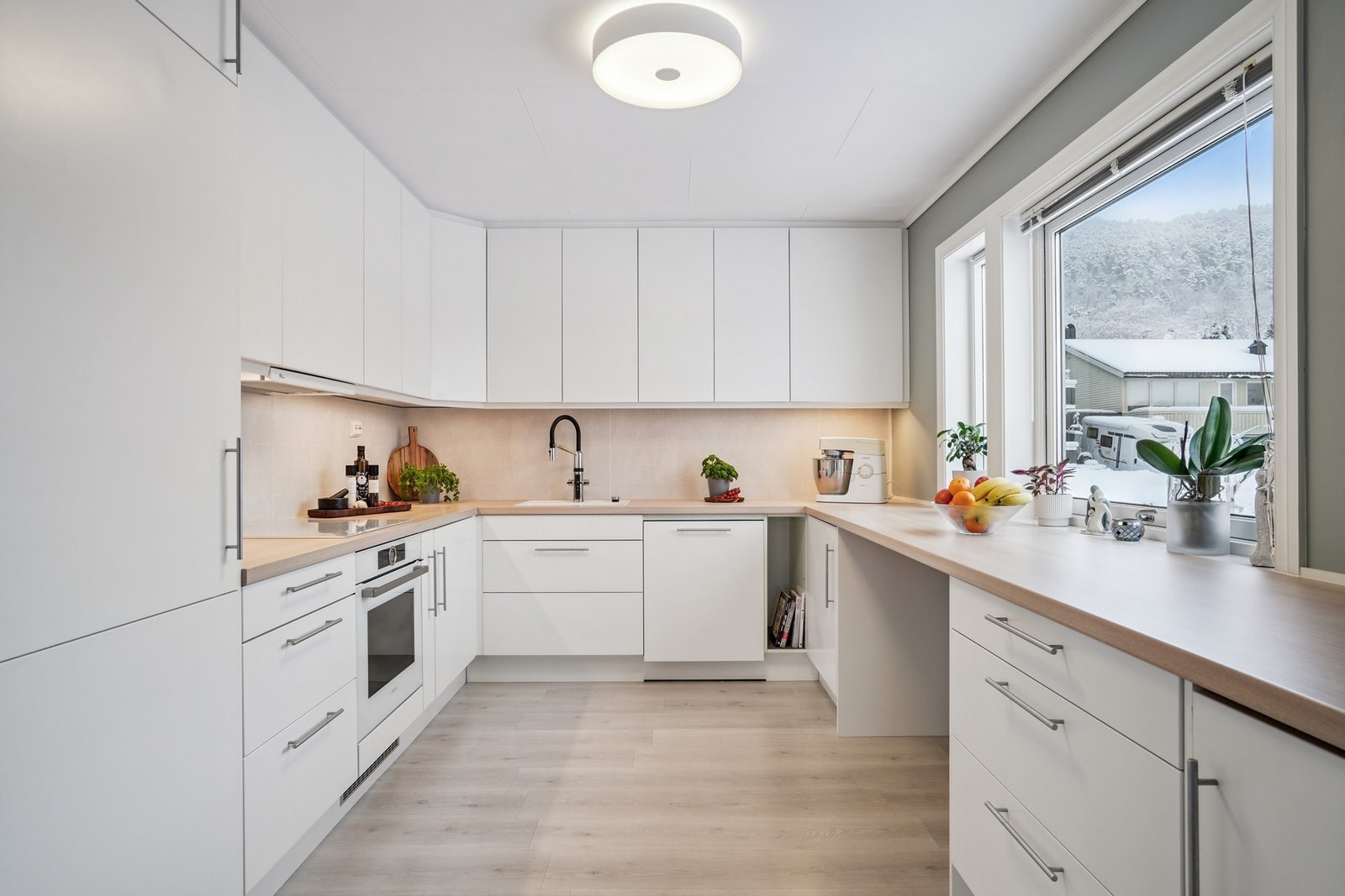 Pent og velutstyrt kjøkken fra Epoq med lyse slette fronter og laminat benkeplate. Belysning under overskap. Galleribilde