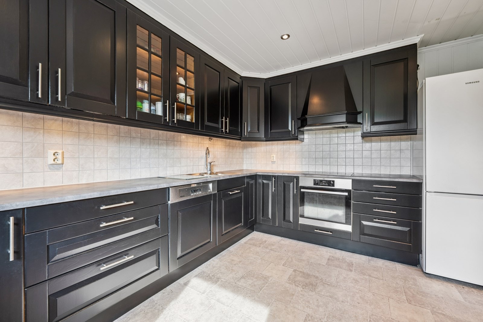 Delikat kjøkken med sorte fronter og integrerte hvitevarer. Frittstående kjøleskap Galleribilde