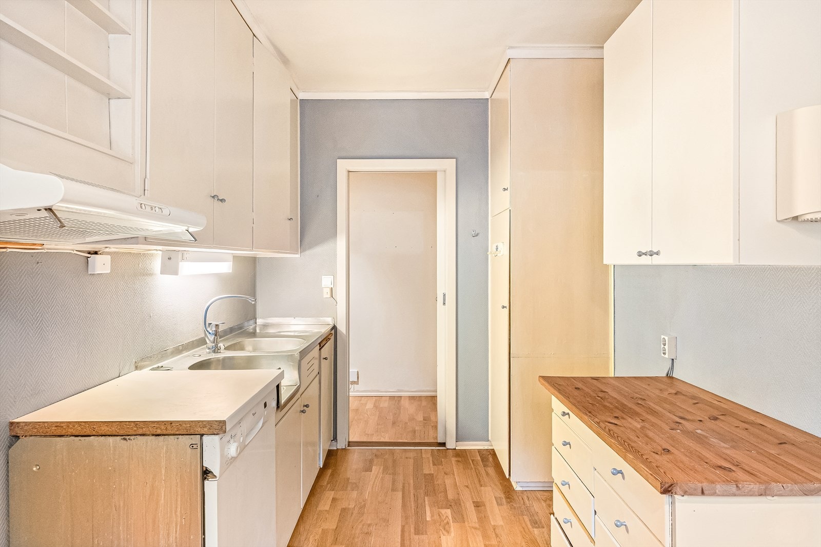 Det er eldre kjøkkeninnredning med slette fronter. Inneholder: laminat/heltre benkeplate, stålvask, ventilator med avtrekk ut og opplegg for oppvaskmaskin. Galleribilde