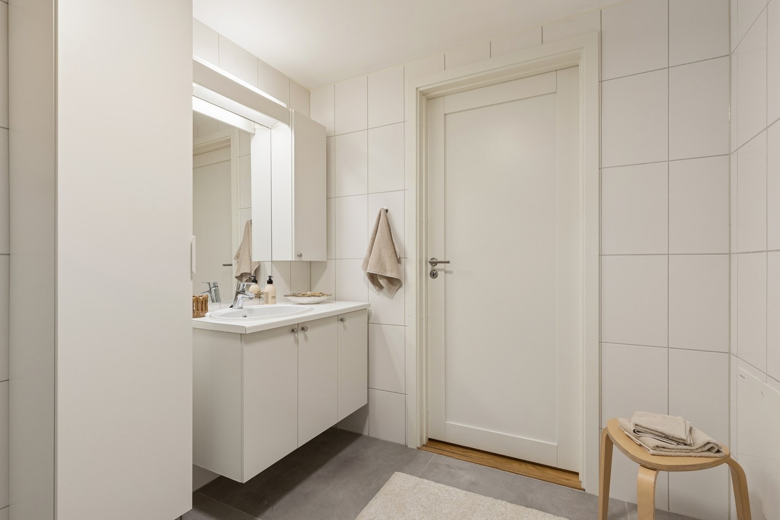 Badet er innredet med heldekkende servant, speil, høyskap, vegghengt toalett og dusjhjørne. Galleribilde