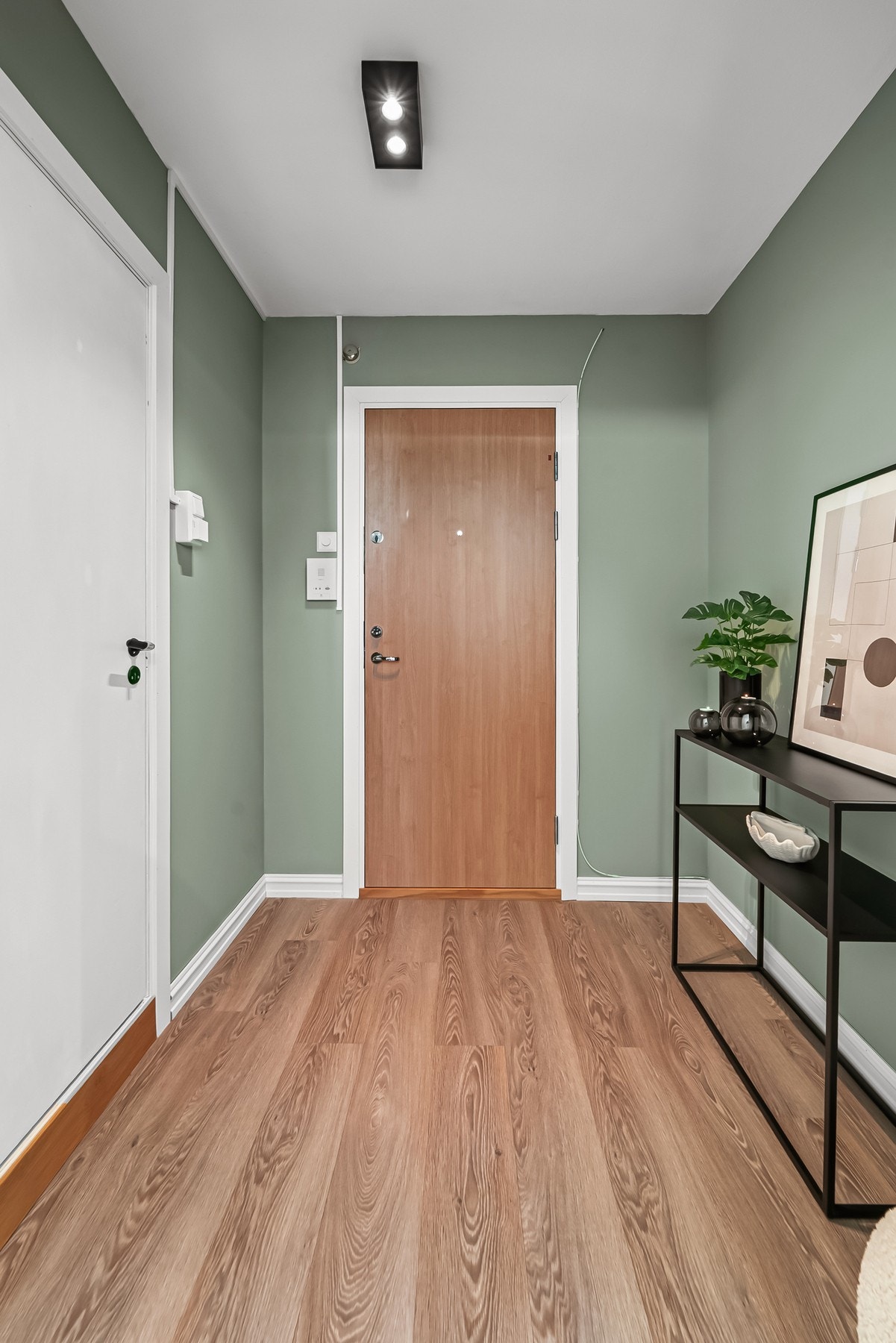 Romslig entrè med plass for garderobeløsning. Gangen er blitt pusset opp i nyere tid, og ytterdøren av massiv tre ble skiftet i 2025 i regi av brl. Ved døren er det montert dørcalling. Galleribilde