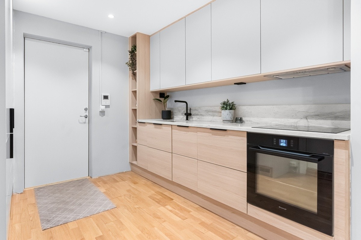 Et lyst og moderne oppholdsrom med åpen løsning mellom stue og kjøkken. Store vinduer gir godt med dagslys, og rommet er innredet med nøytrale farger som gir en luftig følelse. Galleribilde