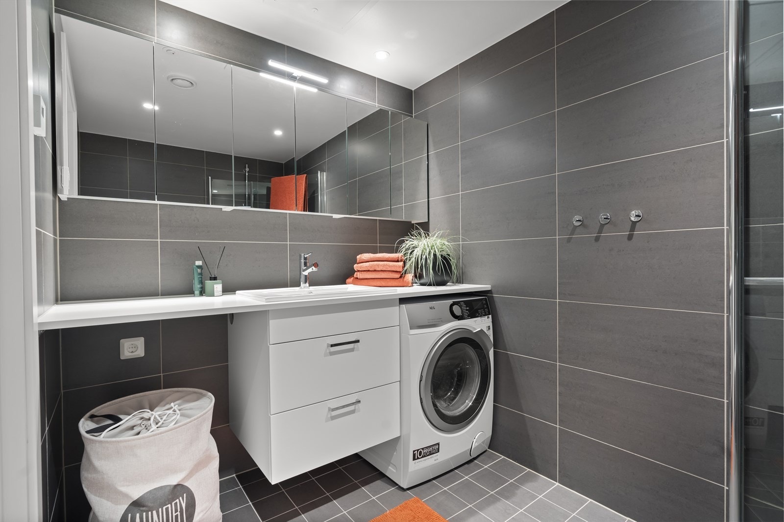 Delikat baderom med store fliser på veggene og litt mindre fliser på gulvet i en nydelig gråtone. Badet har opplegg for vaskemaskin og tørketrommel, samt lun gulvvarme som sørger for en behagelig atmosfære. Galleribilde