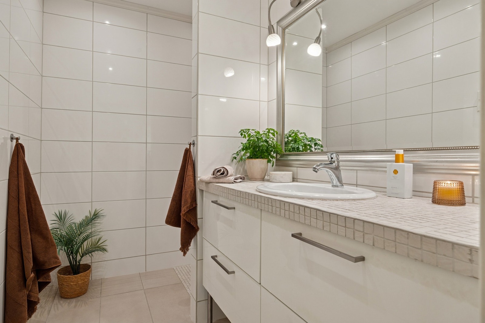 Et lyst og innbydende bad med tidløst design og gulvvarme. Store hvite fliser gir et rent uttrykk, mens innredningen med heldekkende servant og speil med belysning skaper en elegant helhet. Galleribilde