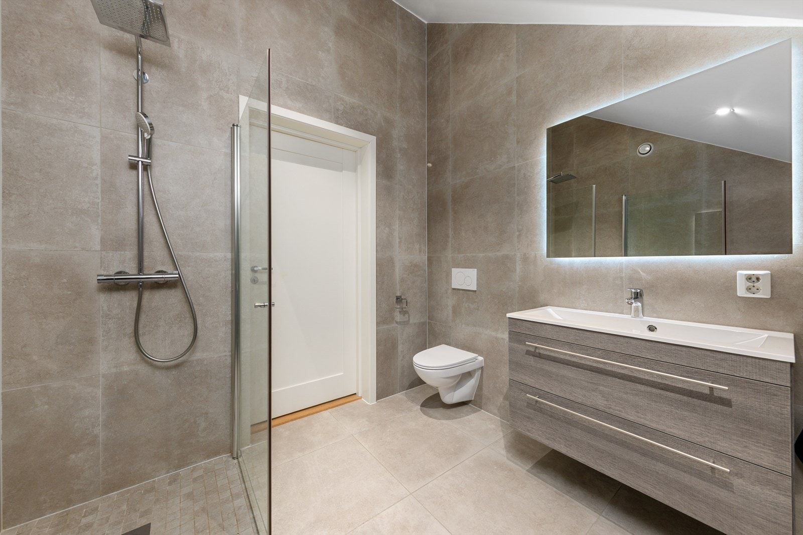 Badet i nedre plan er innredet med servant nedfelt i baderomsinnredning, veggmontert toalett og et dusjhjørne med dusjvegger. Galleribilde