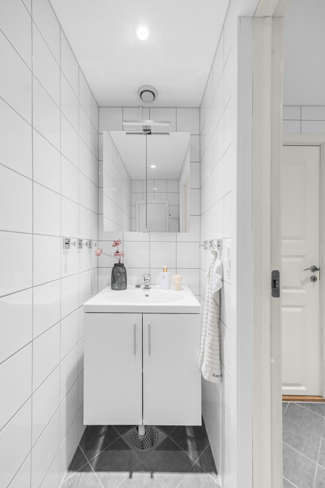 Separat toalettrom utstyrt med et vegghengt toalett med innebygget sisterne, et servantskap med ett-greps blandebatteri og et speilskap. Galleribilde