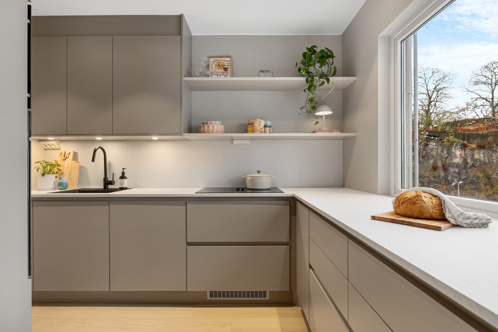 Dette stilrene kjøkkenet med innredning fra HTH fremstår som både moderne og funksjonelt, med rene linjer og gjennomtenkte løsninger. De glatte, matte frontene i en lun, nøytral tone gir et tidløst uttrykk, kombinert med den lyse, laminerte benkeplaten Galleribilde