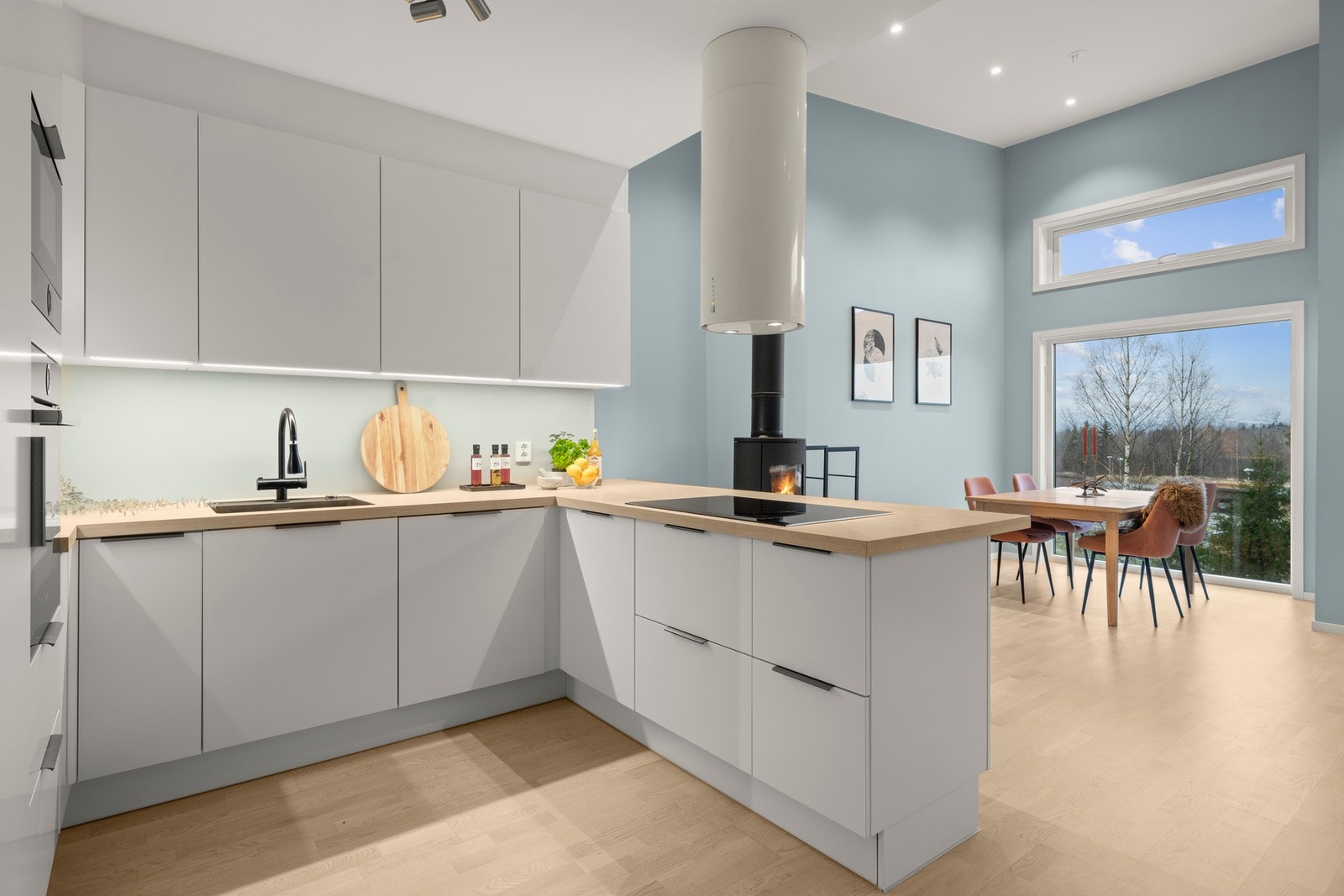 Kjøkkenet er bygget opp rundt en romslig kjøkkenøy som binder matlaging, oppholdsrom og spiseplass naturlig sammen. Løsningen gir en god flyt mellom sonene og gjør kjøkkenet til et sosialt midtpunkt, samtidig som det er rikelig med arbeidsflate og oppbeva Galleribilde