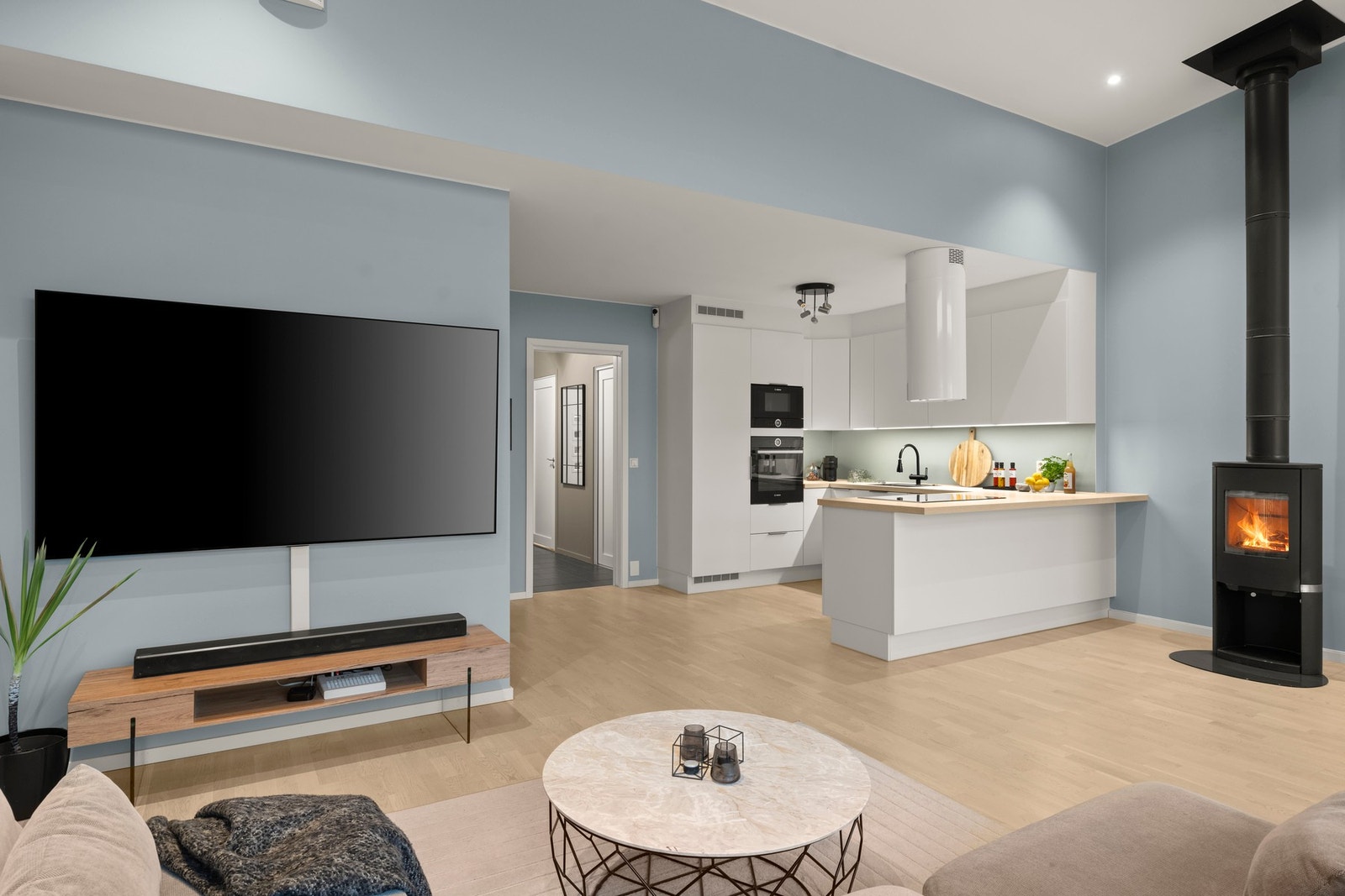 Gjennomførte oppholdsrom med stilren overgang mellom kjøkken og stue. Den moderne kjøkkenøya, integrerte hvitevarer og peisovn gir rommet et eksklusivt preg og understreker boligens moderne uttrykk. Galleribilde