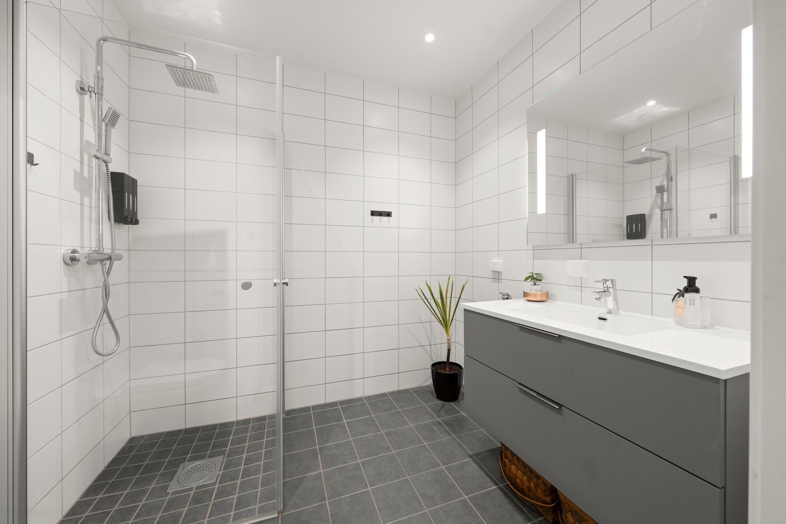 Stilrent og romslig bad i 1. etasje med tidløst flisevalg, dusjnisje med glassvegger og praktisk baderomsinnredning. Et gjennomført rom som kombinerer funksjonalitet med et moderne uttrykk. Galleribilde