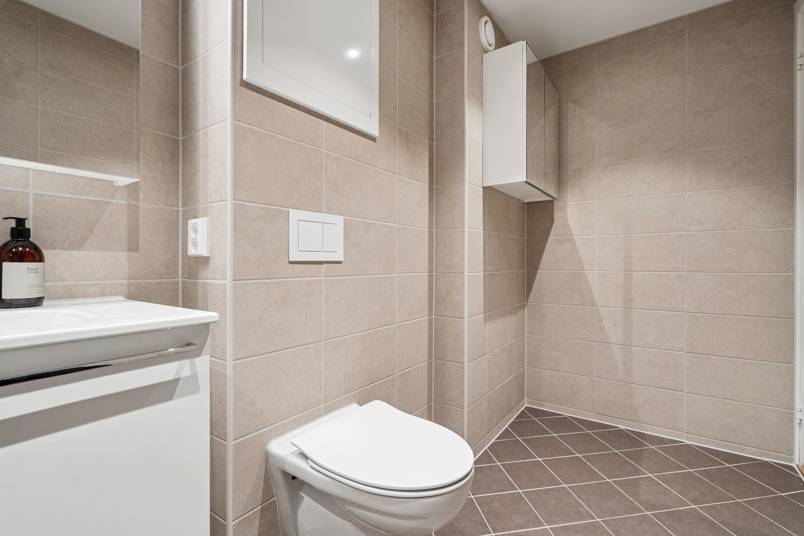 Baderomsinnredningen består av vegghengt toalett med integrert sisterne, servant med underskap, speilskap med belysning, og dusjhjørne med innfellbare glassdører Galleribilde