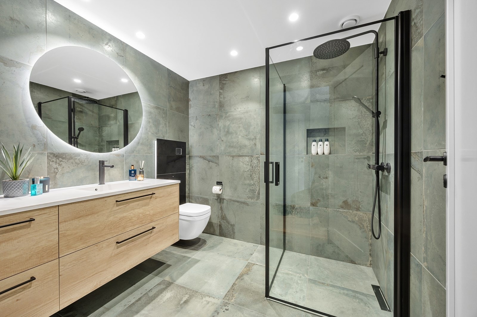 Badet er utstyrt med en vegghengt toalett og en elegant servantinnredning med skuffer, speil og dusjone med innfellbare glassvegger. Galleribilde