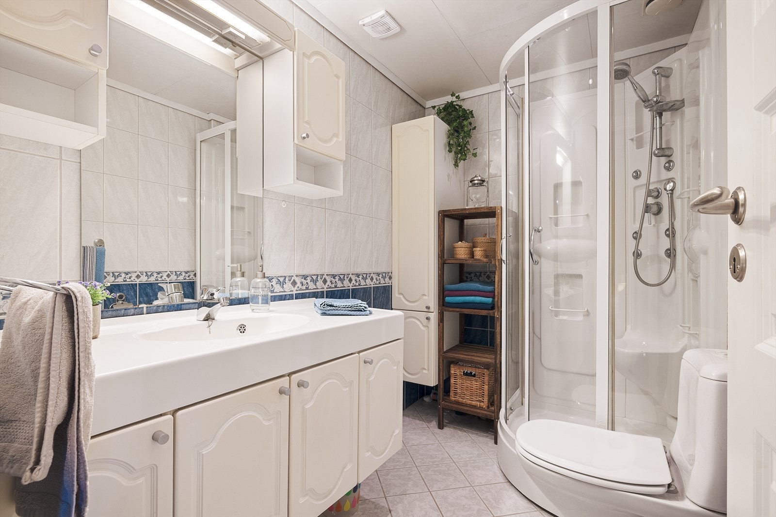 Badet er fliselagt og består av speil, servant med seksjon, toalett og dusjkabinett. Galleribilde