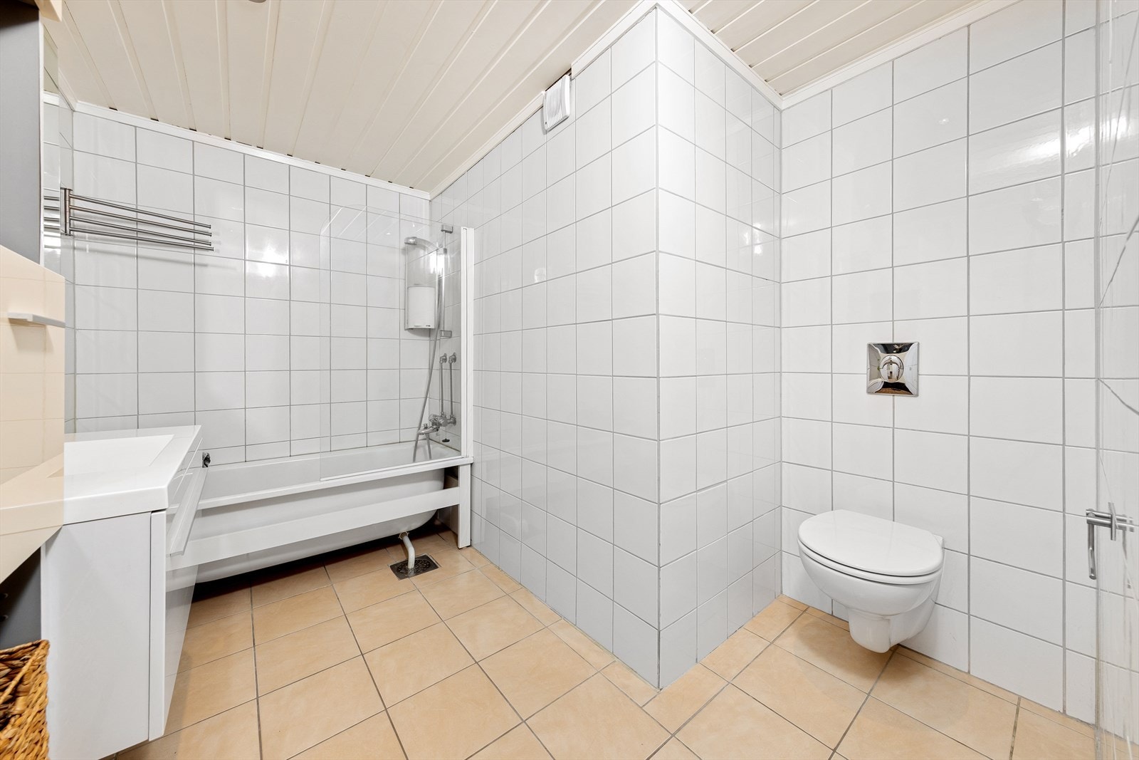 Lyst flislagt bad med behagelige varmekabler i gulv. Badet er utstyrt med badekar med dusjløsning og vegghengt toalett. Galleribilde