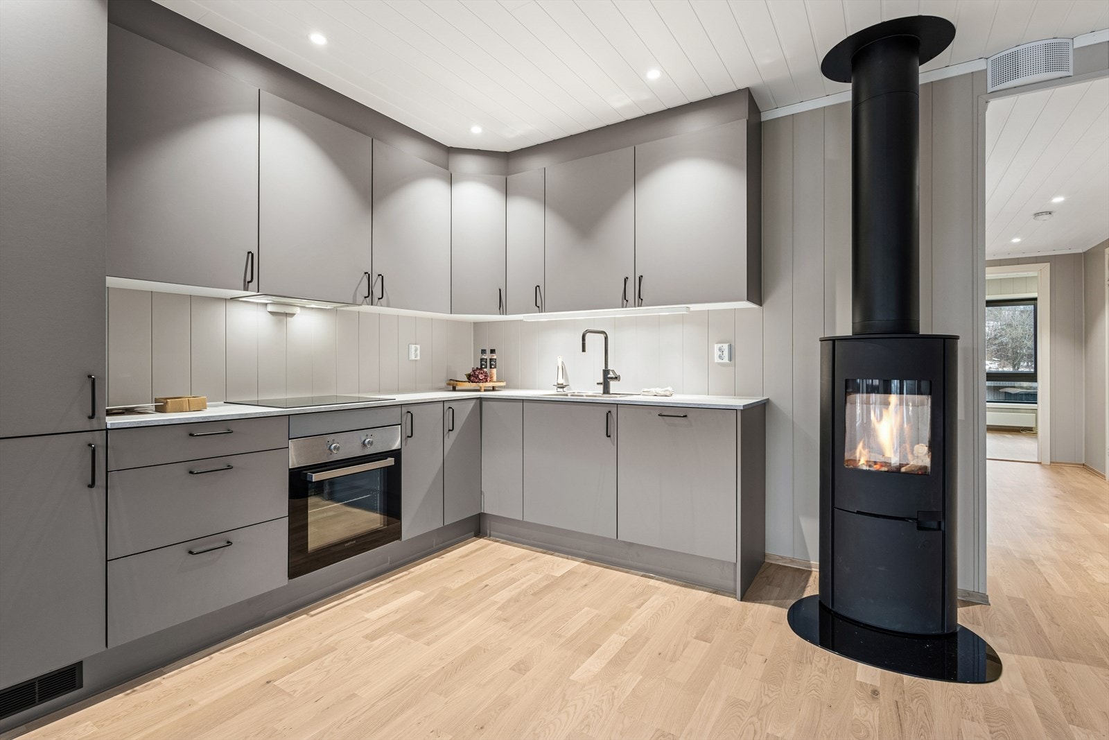 Innredningen består av glatte, grå fronter og laminert benkeplate med kjøkkenkum. Det er belysning over benkeplaten. Galleribilde