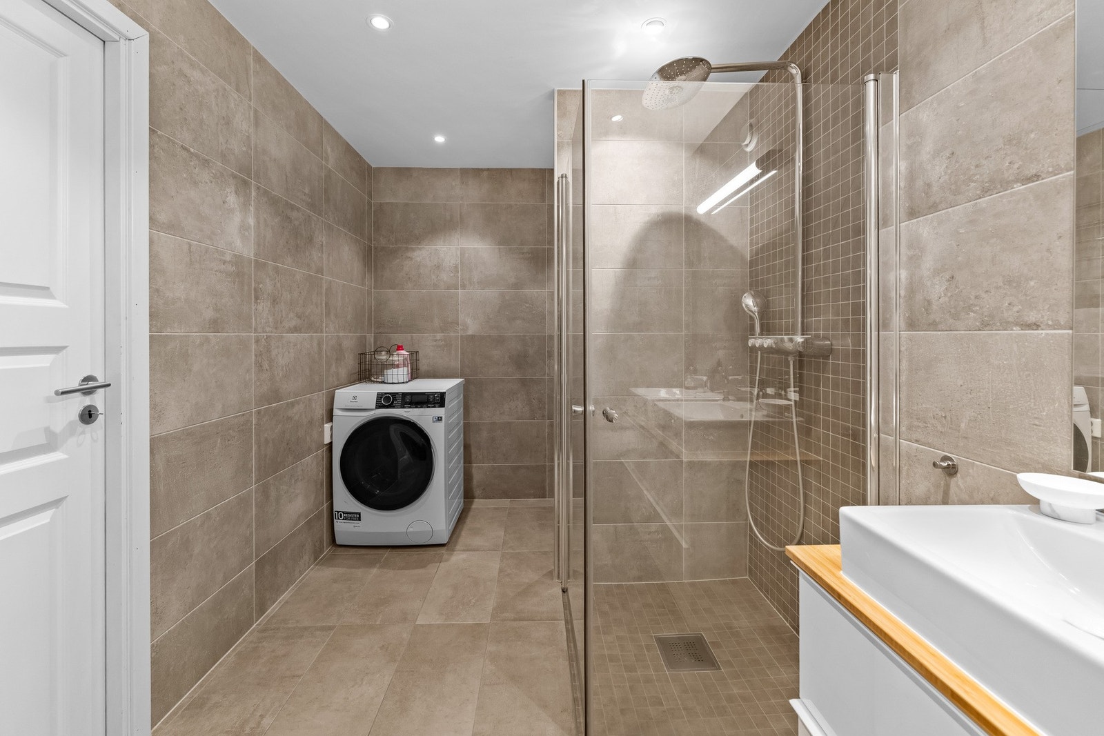 Baderommet er flistlagt og har 2 servanter, servantskap, veggmontert wc, dusjhjørne med innfellbare dører og opplegg for vaskemaskin Galleribilde