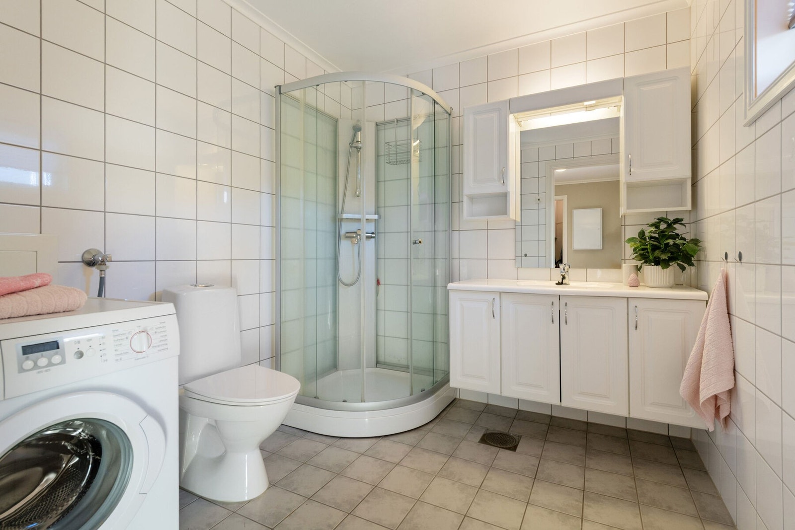 Flislagt bad med varmekabler. Badet er innredet med dusjkabinett, servant med skap, toalett og vaskemaskin. Galleribilde