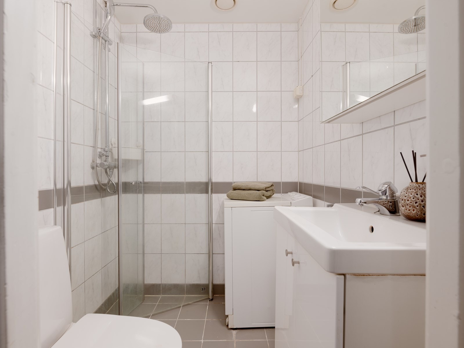 Badet består av klosett, innfellbare dusjdører, servant med underskap og overskap med speilfronter. Galleribilde