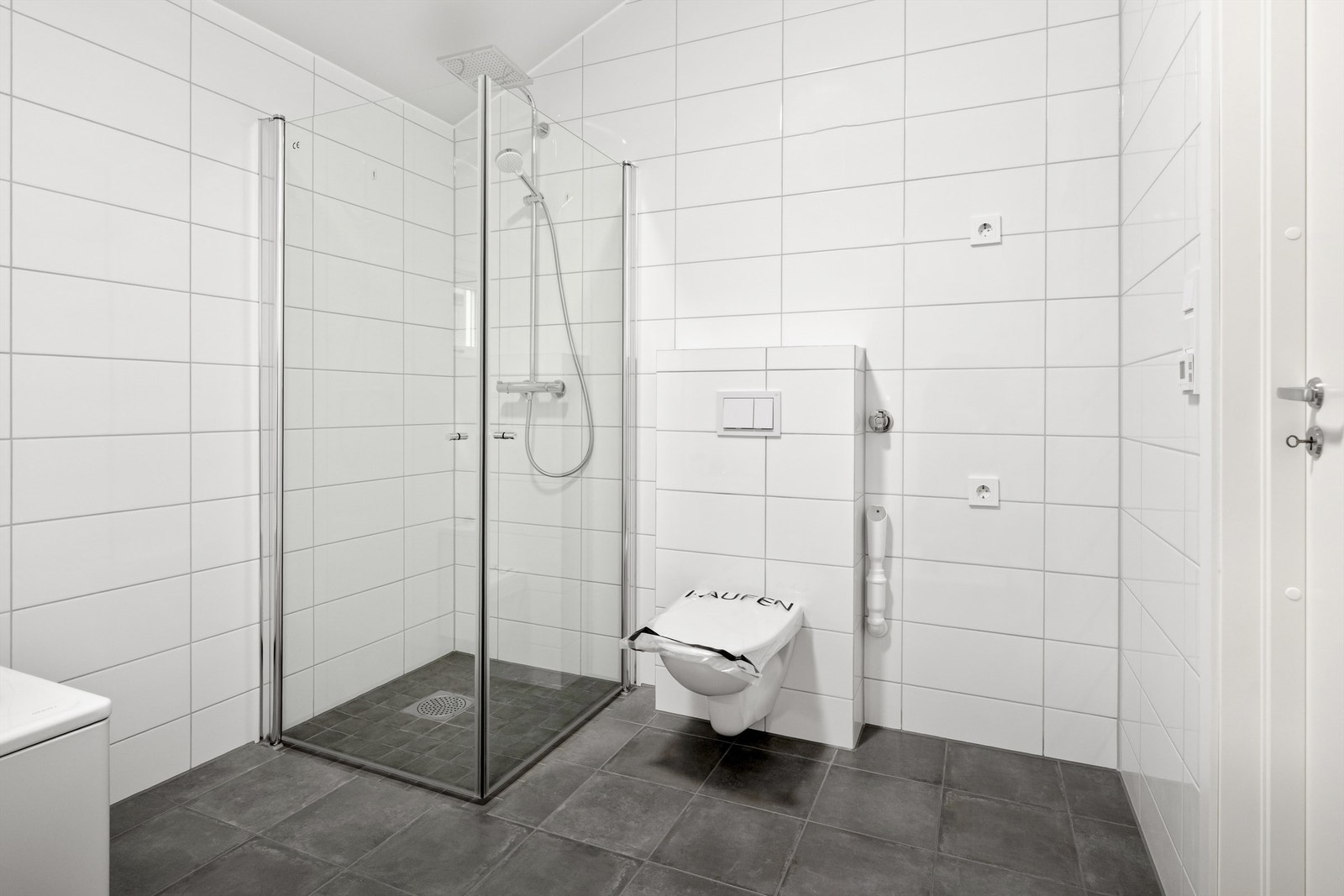 Flott flislagt bad med vegghengt toalett, dusj og badekar Galleribilde