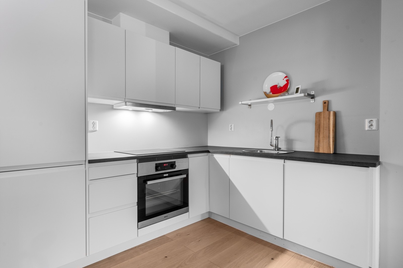 Innredningen har hvite, glatte fronter fra byggeåret og laminatbenkeplater som både er stilrene og lettstelte. Her finner du nedfelt oppvaskkum med ettgreps armatur, integrert komfyr, induksjonstopp med komfyrvakt og mekanisk ventilator. Galleribilde