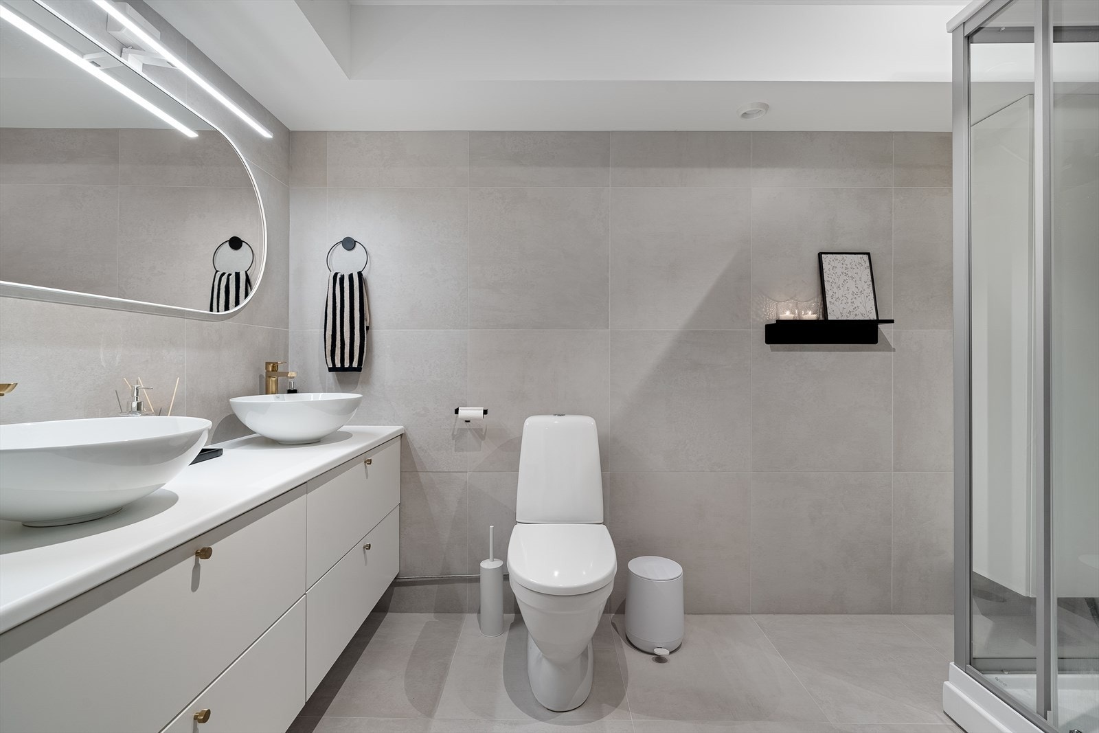 Flott flislagt bad med toalett, dobbel servant med innredning og dusjkabinett. Galleribilde