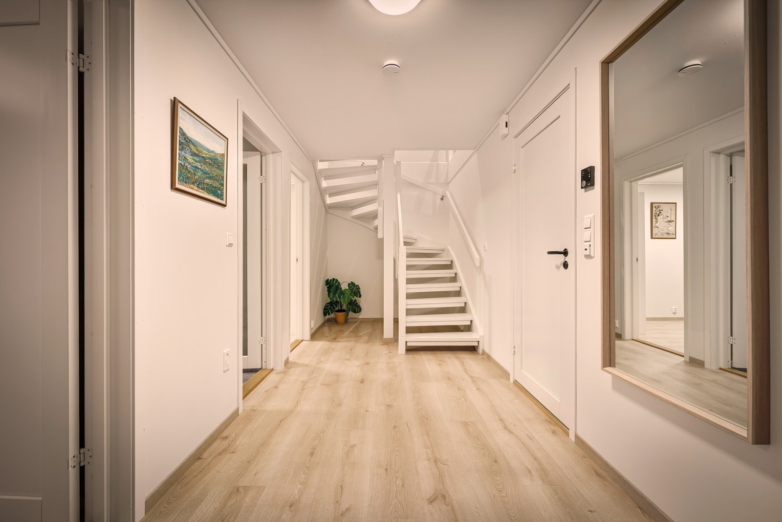 Bildet viser gangen nede med trapp til etasjen over. Overflatene er malt i en nøytral fargetone. Galleribilde