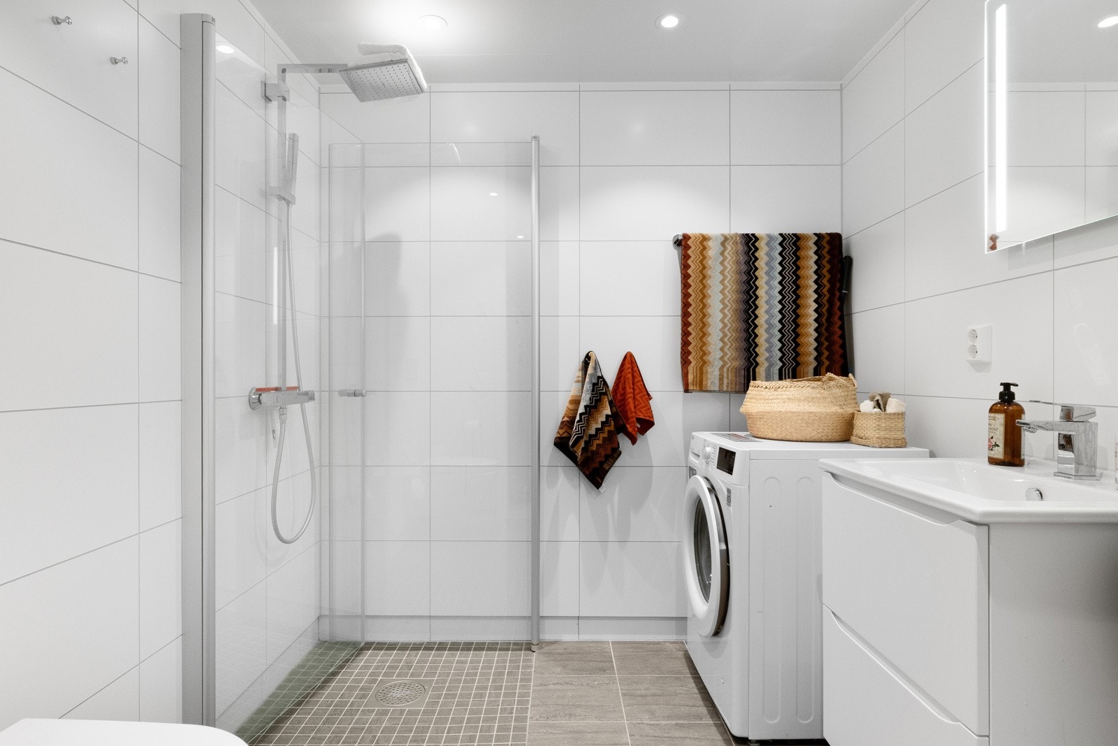 Leiligheten har to flislagte bad, dette er det største. Det har dusjhjørne, vegghengt wc, opplegg for vaskemaskin og downlights i taket. Galleribilde