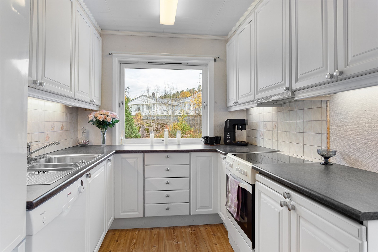 Flislagte felt på vegg over benkeplater av laminat og lysarmaturer under overskap Galleribilde