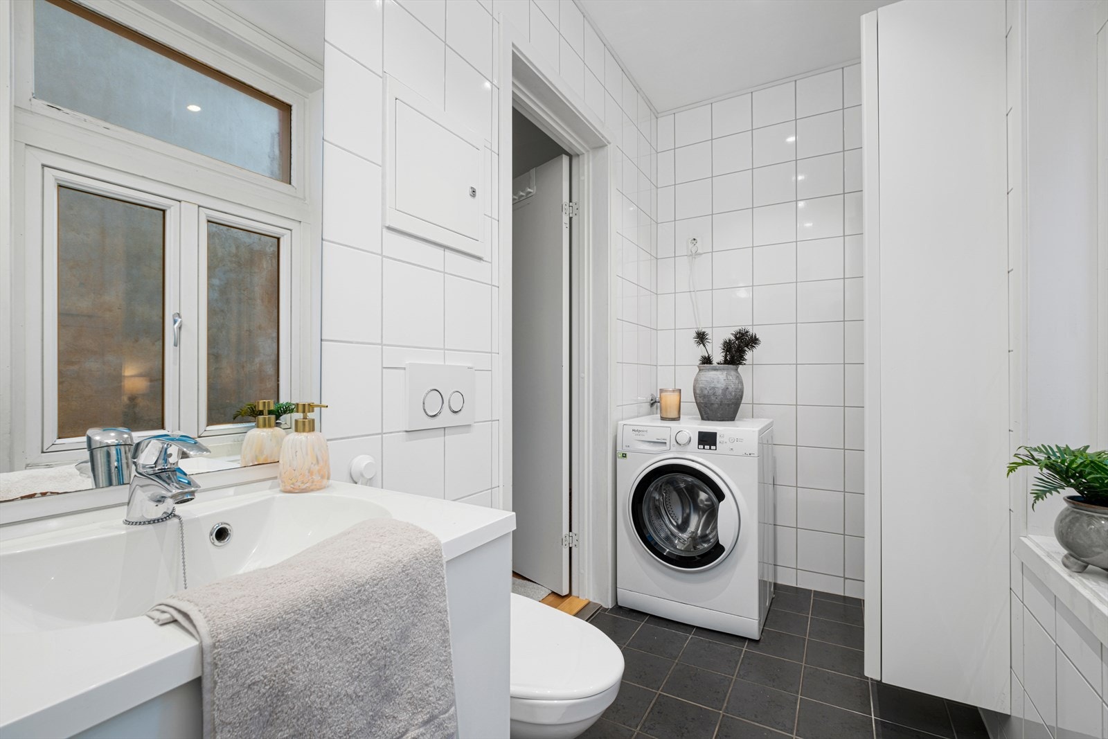 Badet er innredet med dusjvegger av glass og dusjgarnityr på vegg, veggmontert toalett, innredning med servant og opplegg for vaskemaskin. Galleribilde