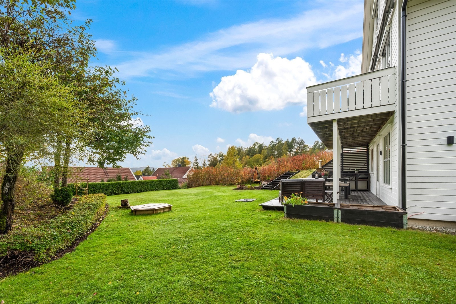 Skrånende tomt som er pent opparbeidet med gressplen, hekk, barkebed og diverse beplantninger Galleribilde