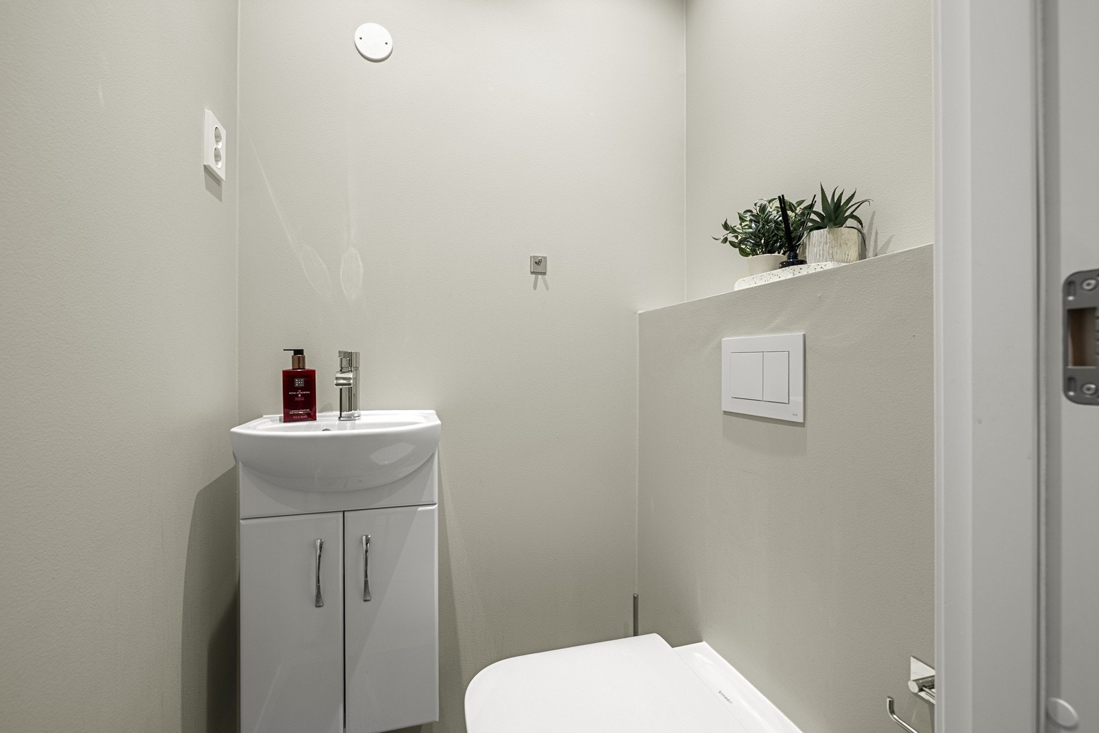 Toalettrom med flislagt gulv, vegghengt toalett og servant. Malte overflater og downlights i tak. Galleribilde