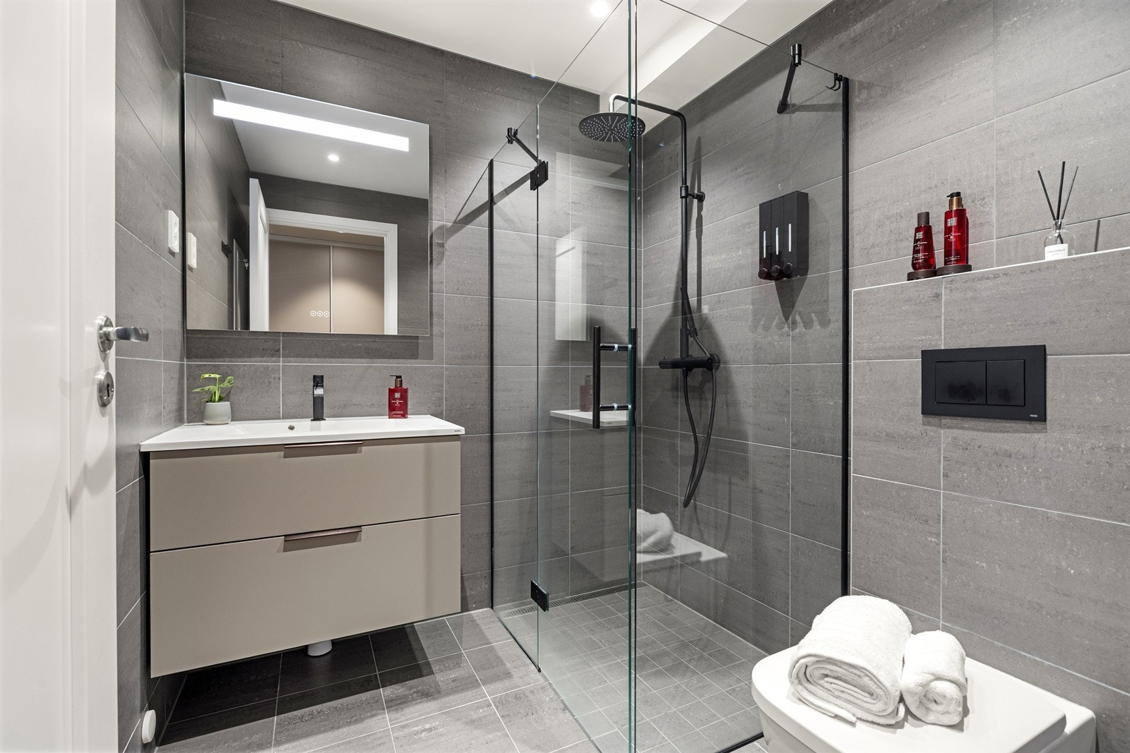 Delikat, helfliset en-suite baderom med vannbåren gulvvarme, vegghengt toalett, servant med skuffer og dusjhjørne med regnfallsdusj i sort krom Galleribilde