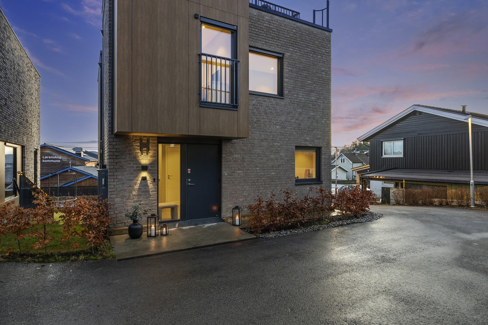 Stilren fasade i kombinasjon av teglstein og fasadeplater, med utvendig veggbelysning på alle fire sider som fremhever boligen på kveldstid Galleribilde