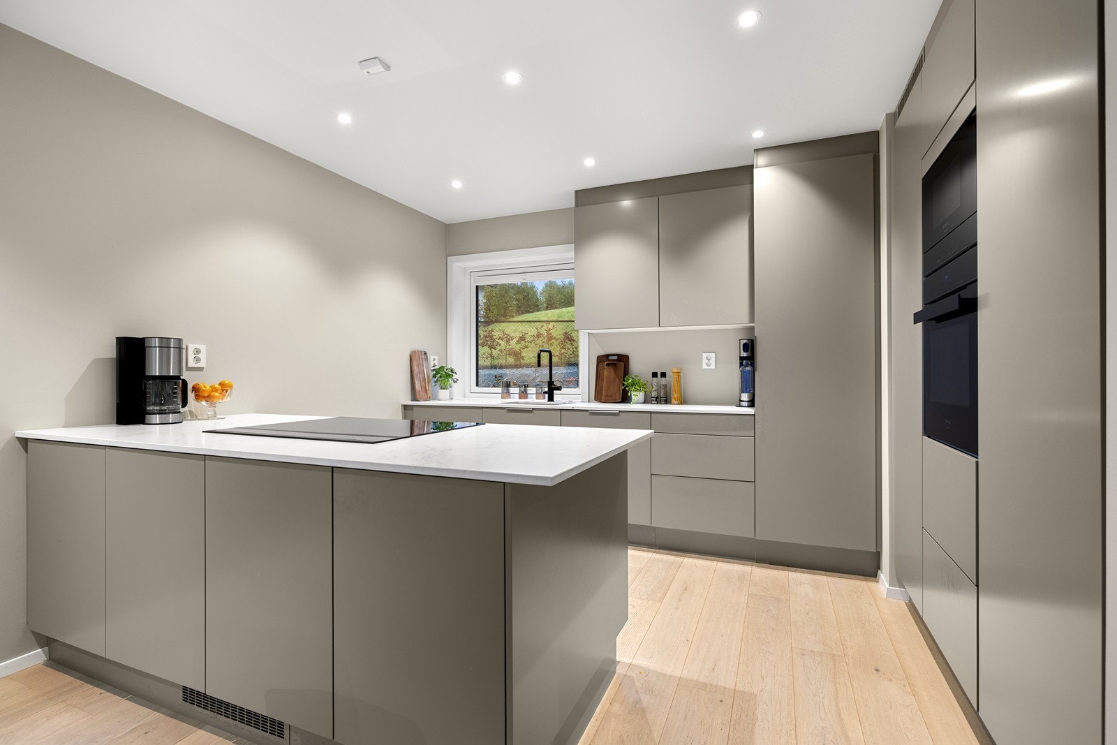 Kjøkkenet har en stilren innredning med glatte fronter og en solid benkeplate i keramikk. Galleribilde