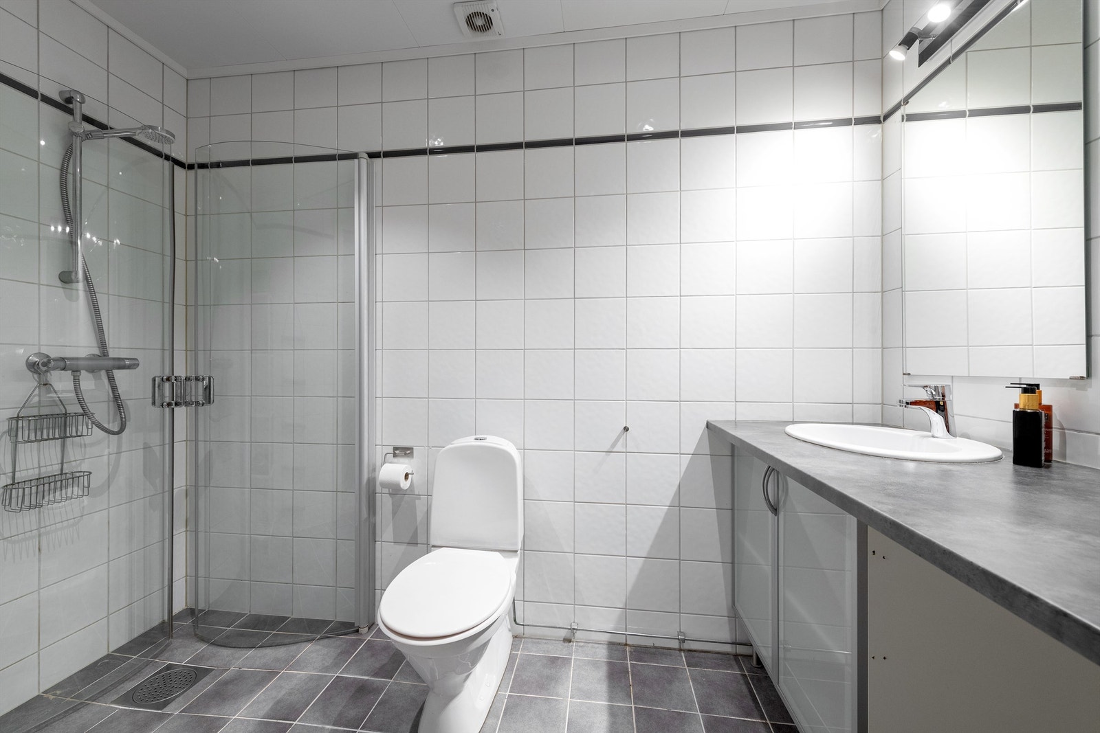 Flislagt bad med vannbåren gulvvarme. Innredning med ovenpåliggende servant. Speil med overlys og stikkontakt over servant Galleribilde