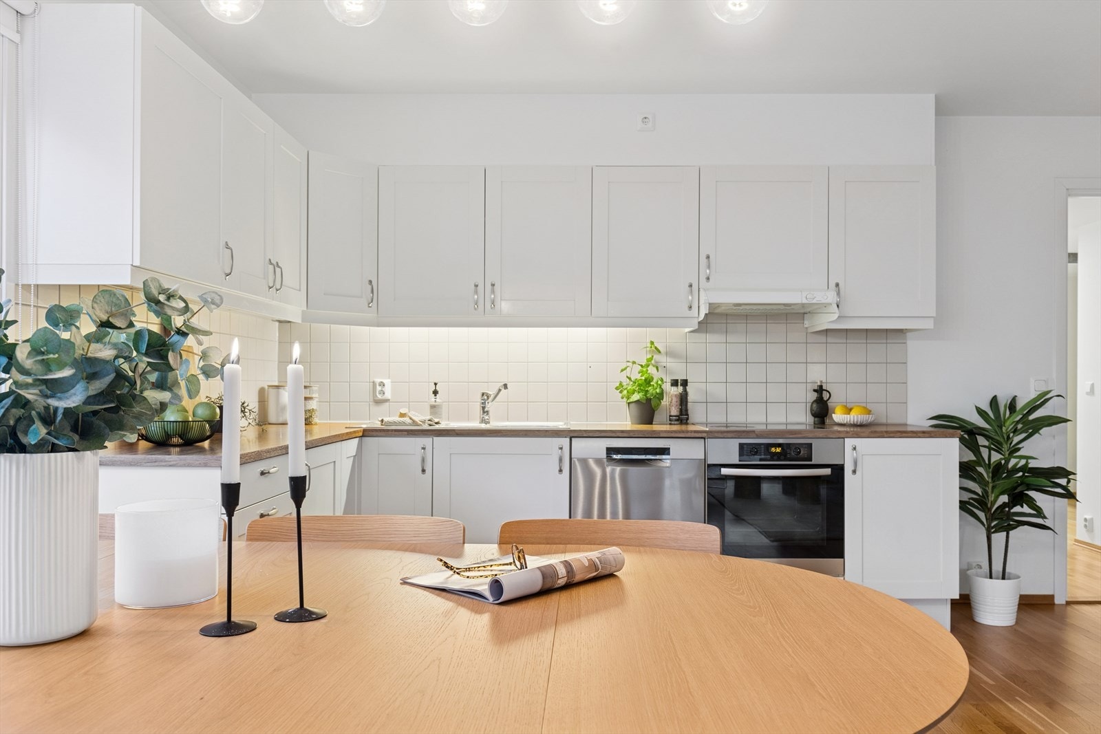 Kjøkken med hvite profilerte fronter og laminat benkeplate med oppvaskkum samt flisbelagt felt mellom overskap og underskap. Galleribilde