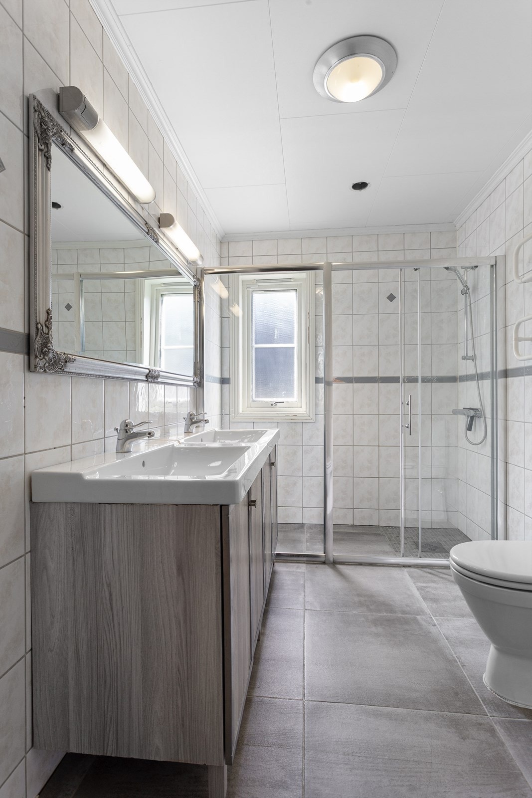 Flislagt bad i 1. etasje med dobbelservant over gulvstående servantinnredning i glatt utførelse Galleribilde