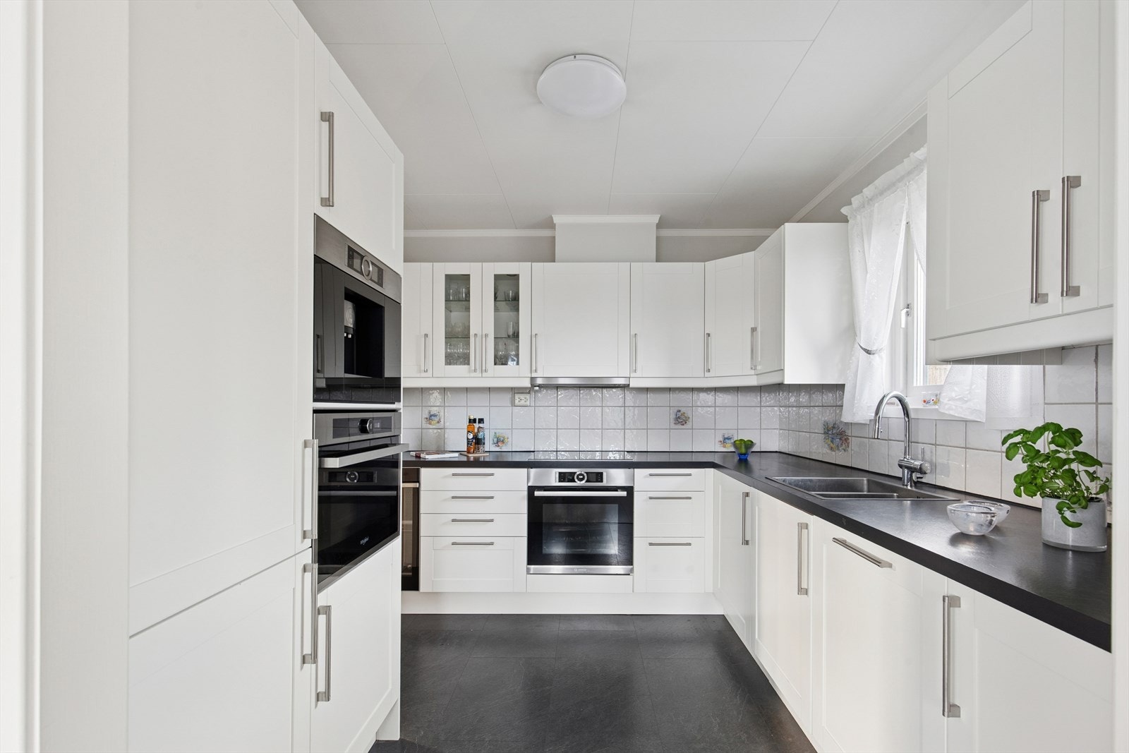 Kjøkkenet fra Montera (2018) har en innredning med ett-speils fronter, laminat benkeplate og fliser over benken. Galleribilde