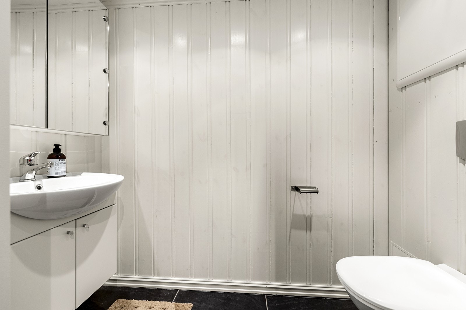 Separat toalettrom med flislagt gulv, vegghengt toalett og servant med skap. Varmekabler i gulv. Galleribilde