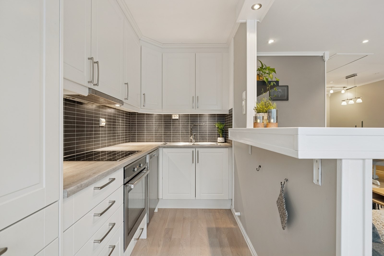 Lyst og funksjonelt kjøkken med klassiske hvite fronter, hvitevarer og stilfull mørk vegg over benk og under overskap. Galleribilde